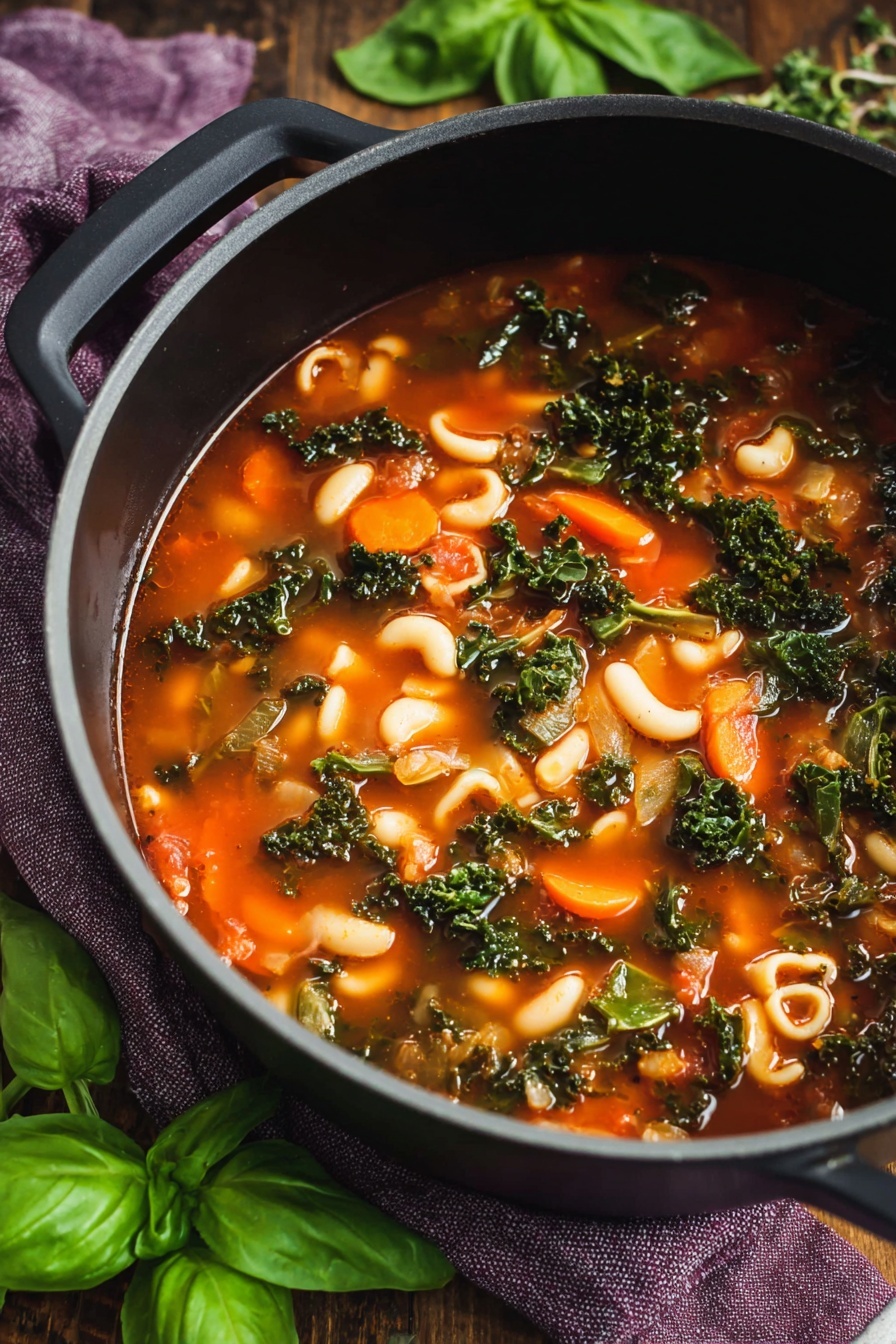 The image shows a bowl of soup filled with several layers: at the bottom, there is a clear reddish broth; next is a mix of white beans, green leafy kale, green beans, orange carrot slices, and small pasta shapes spread evenly. On top, there are white shavings of cheese and fresh bright green basil leaves placed in the center and around the edges of the soup. The soup is served in a white bowl with a scalloped dark blue edge, sitting on a wooden table scattered with fresh basil leaves. Another white bowl with the same soup and a black pot with more soup wrapped in a woven mat are partially visible nearby. The photo taken with an iphone --ar 2:3 --v 7